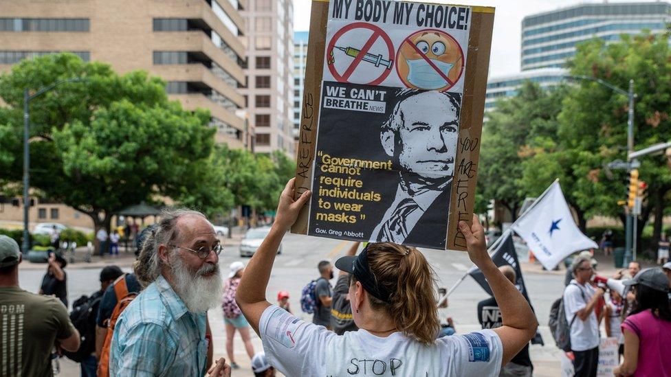 Man talking to a woman holding an anti-face mask sign at a protest