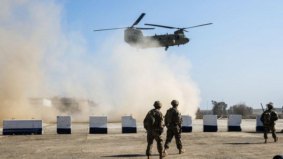 US troops walk as a US Army C-47 Chinook helicopter flies over the village of Oreij, south of Mosul, on February 22, 2017