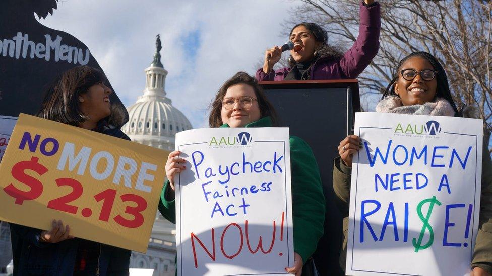 People hold signs saying "no more $2.13" and "women need a raise"