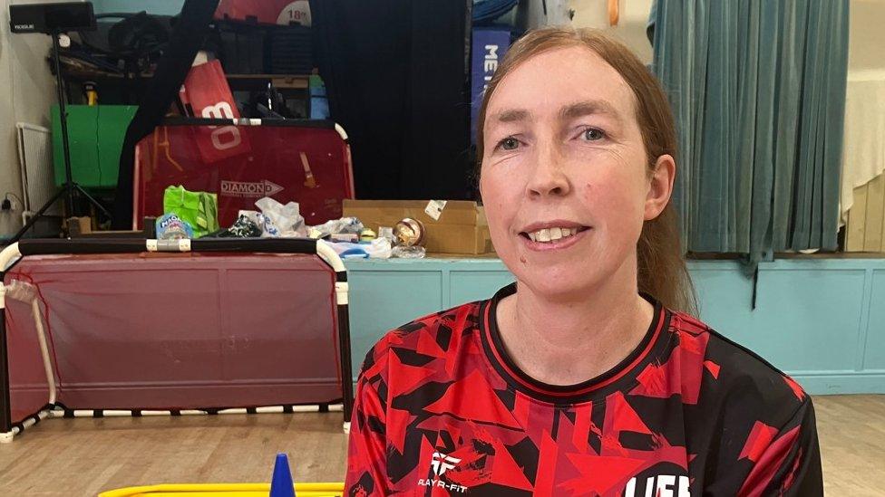 A woman sits in a hall surrounded by sports equipment