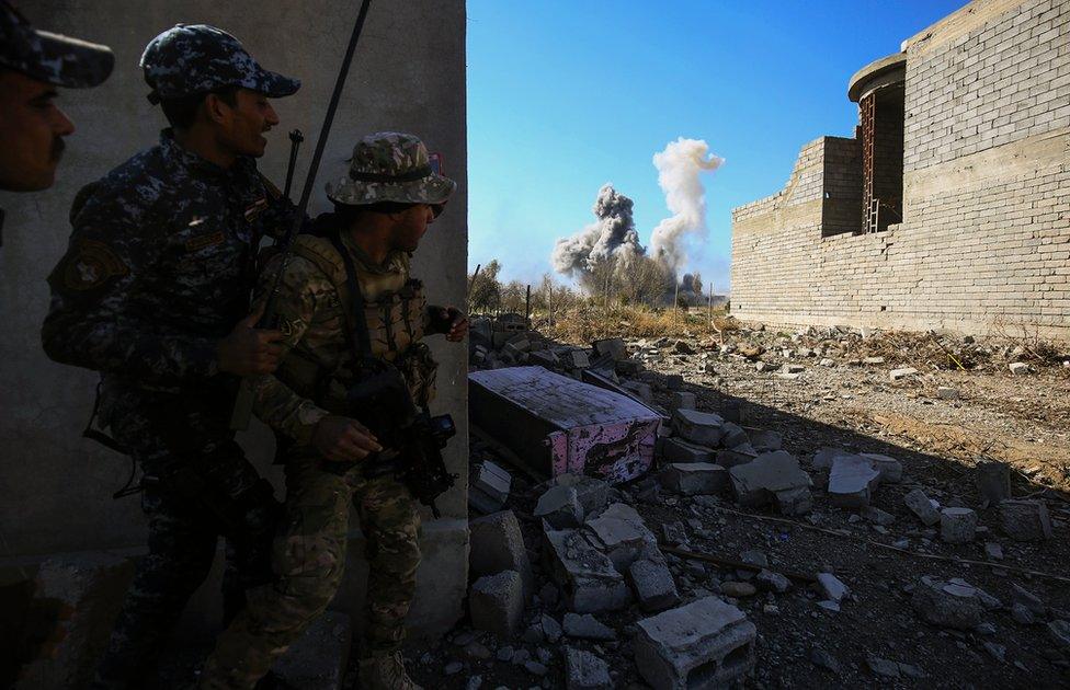 Members of the Iraqi forces take cover as smoke rises in the background during their advance towards Dindan neighborhood in the western half of the northern city of Mosul, as part of the offensive to retake the area from Islamic State (IS) group fighters, on February 25, 2017.