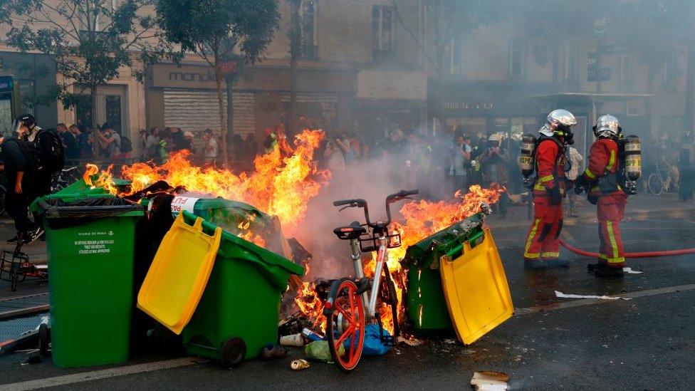 Fire-fighters stand next to bins, rubbish and a bike on fire in the Paris streets