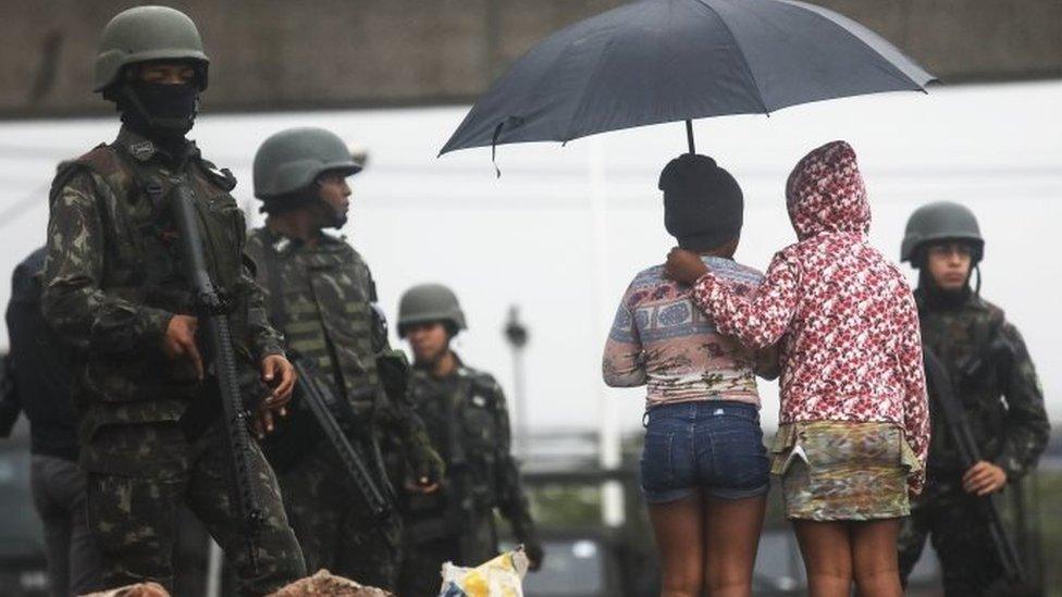 Youngsters stand near Brazilian soldiers during a "Mega Operation" conducted by the Brazilian Armed Forces along with police against gang members in seven of Rio's most violent "favela" communities on August 21, 2017 in Rio de Janeiro, Brazil.