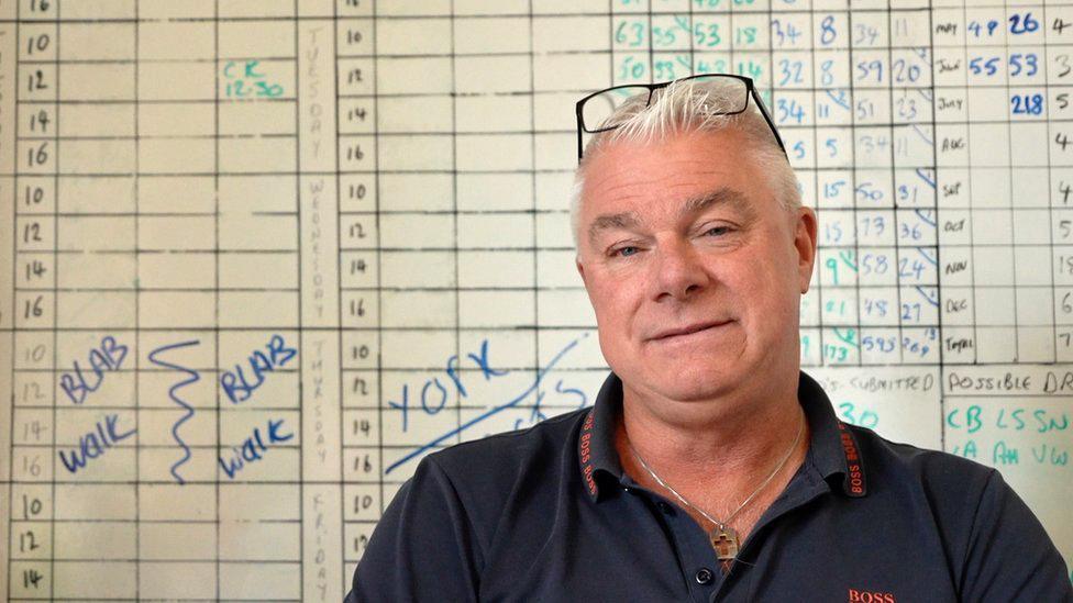 Andrew Sykes sat in front of a wall-mounted calendar