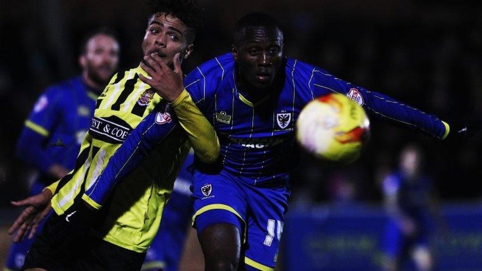 Josh Passley of Dagenham and Redbridge challenges Adebayo Azeez of AFC Wimbledon