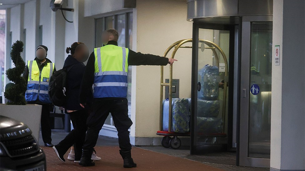 A woman is given instructions by a G4S guard as she arrives at a Heathrow quarantine hotel in February