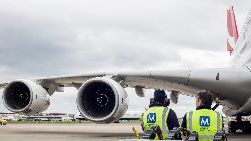 Two ground handling staff standing in front of the wings of an aeroplane