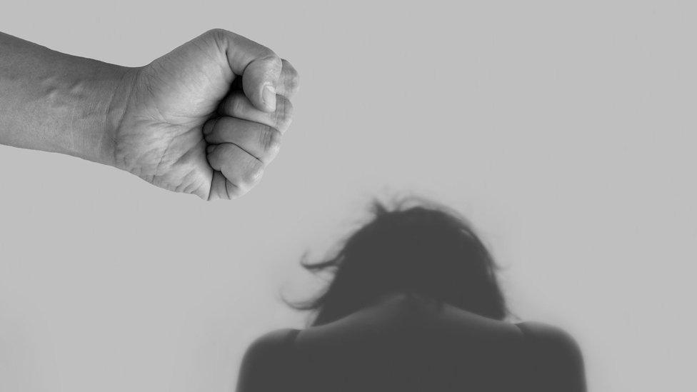 A black and white staged photo of a man's fist with a woman cowering beyond