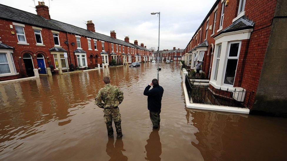 A man and an army personnel look at the flooded street they're standing in