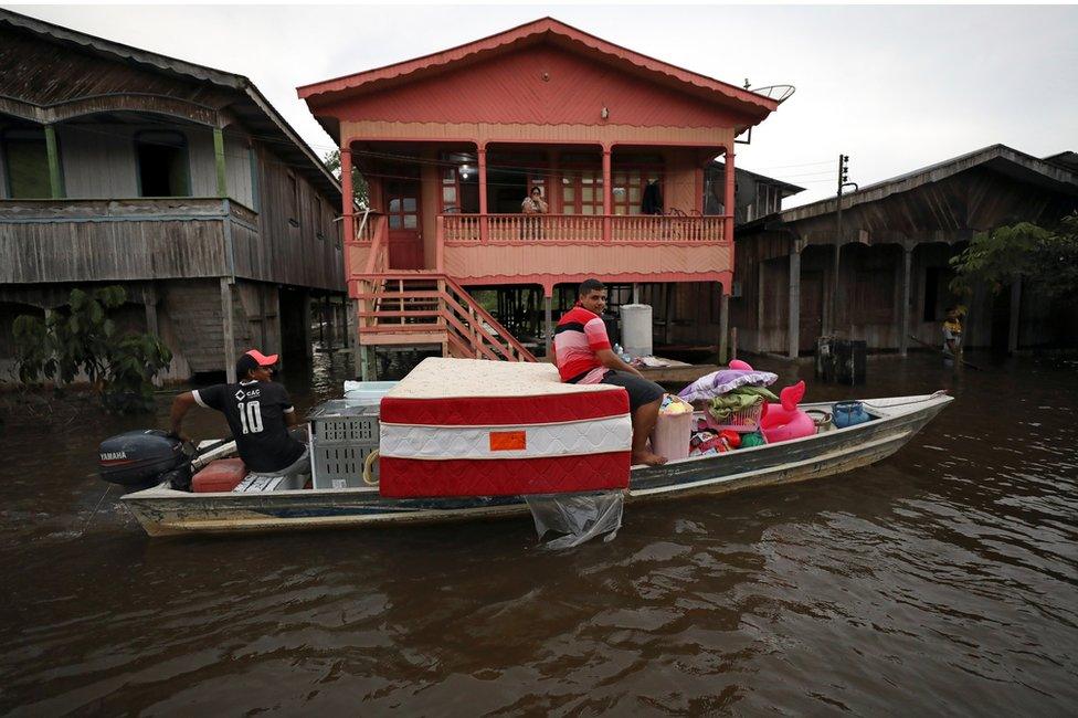 Residents take their belongings on a boat in a street flooded by the rising Solimoes river