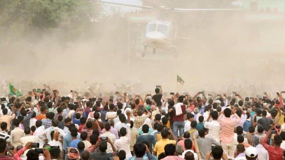 People look on as RJD leader Tejashwi Yadav leaves in a helicopter during an election campaign rally at Masaurhi on October 21, 2020 in Patna