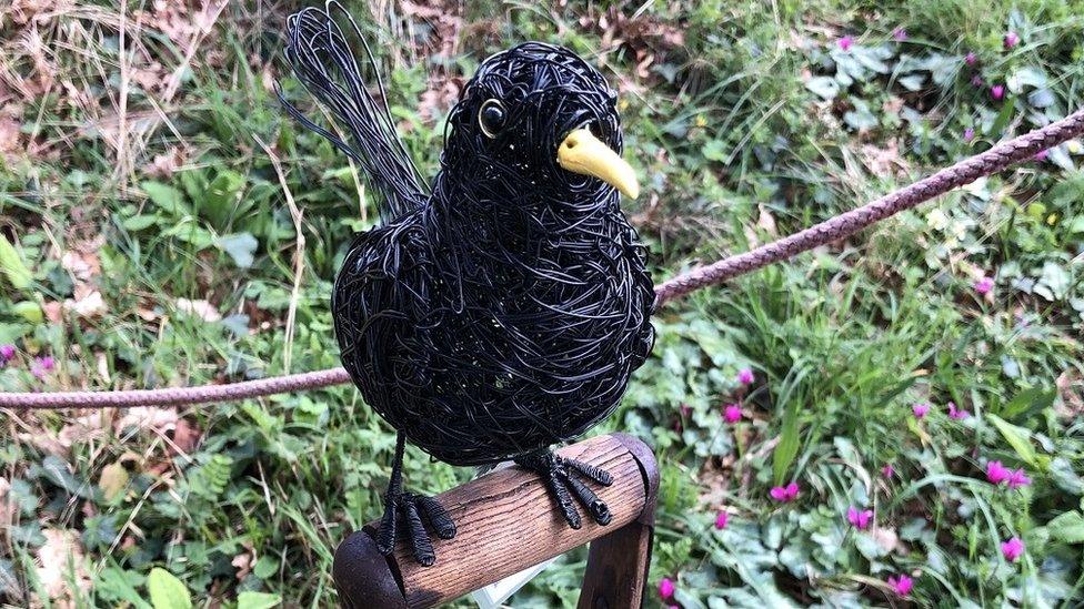 A sculpture of a black bird sitting on a fork handle at Bristol University Botanic Gardens