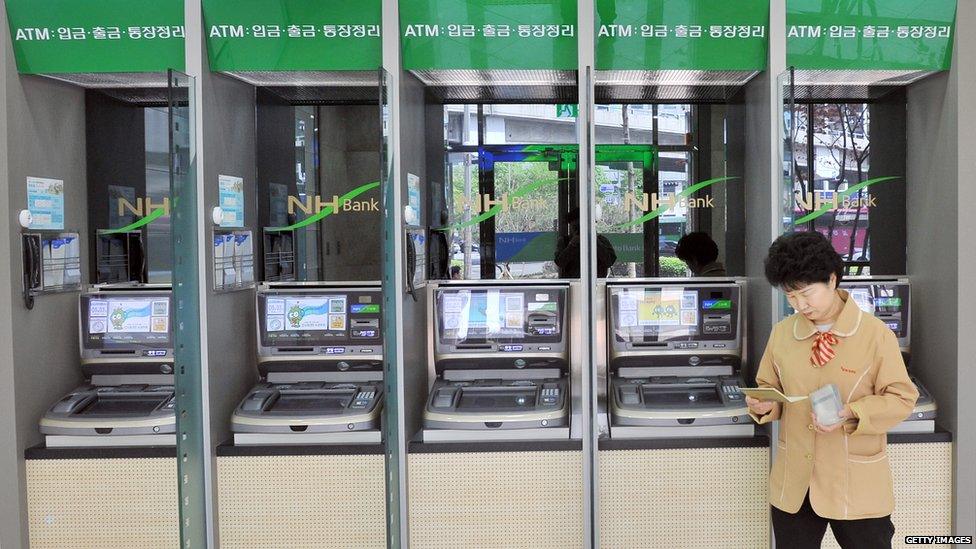 A woman stands in front of a line of ATMs in Seoul