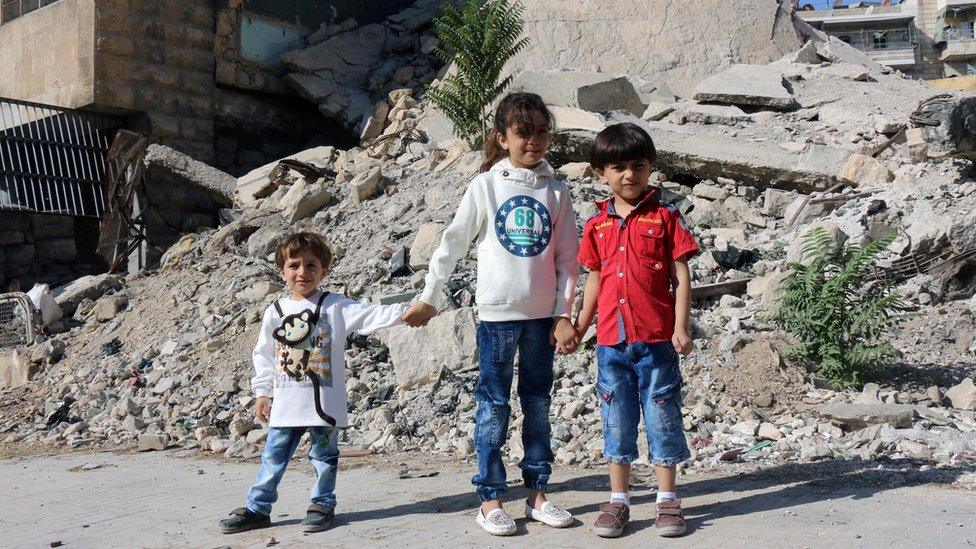 Bana posing for a picture with her brothers amid the rubble of a destroyed building