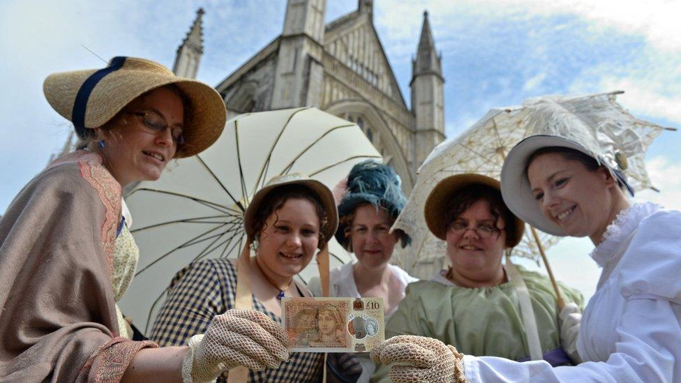 Jane Austen fans in costume pose with the new £10 note in front of Winchester Cathedral where the author is buried