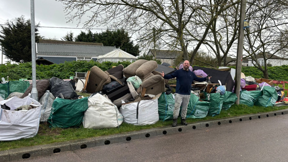 Bradley Thompson stood in front of fly tipping and collected litter