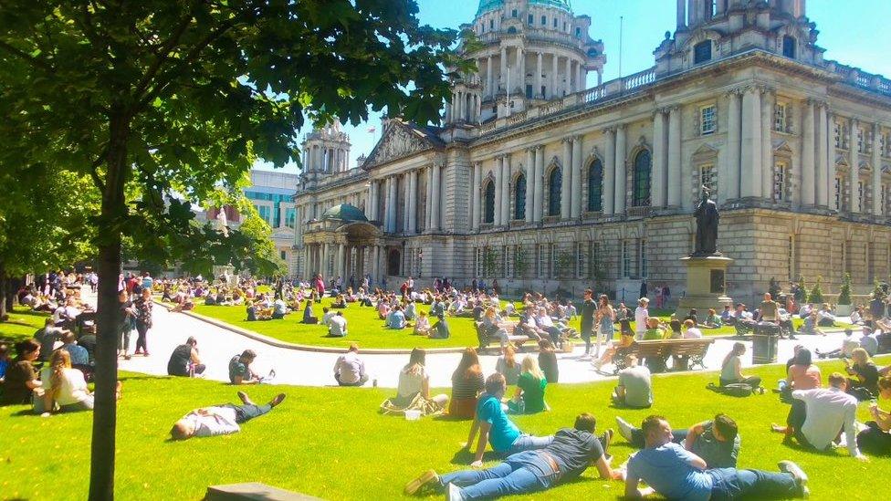 People lie on the lawn at the front of Belfast City Hall enjoying the sun