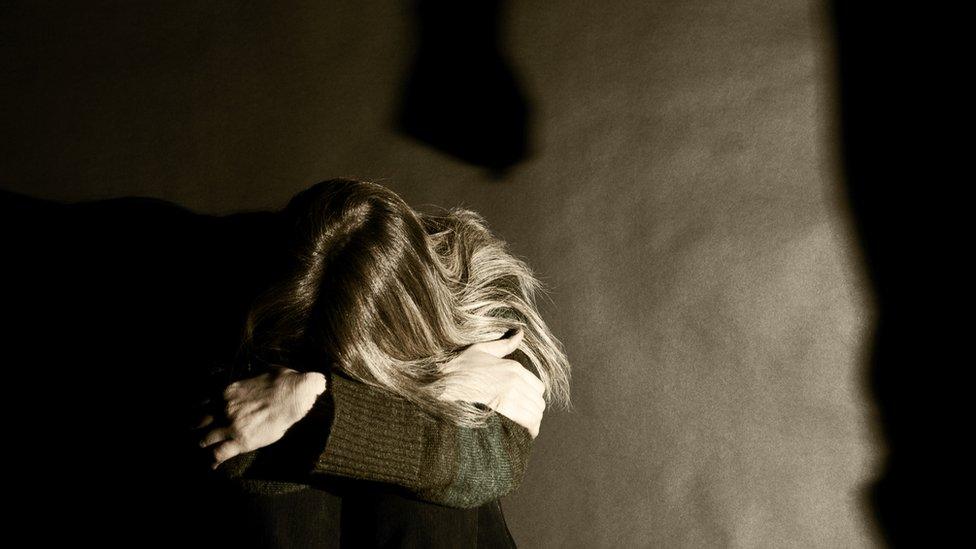 A woman cowering with the shadow of a man's fist on the wall behind her