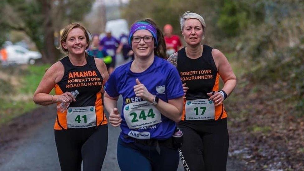 Ruth Coleman in competition kit running on a trail flanked by two other women runners