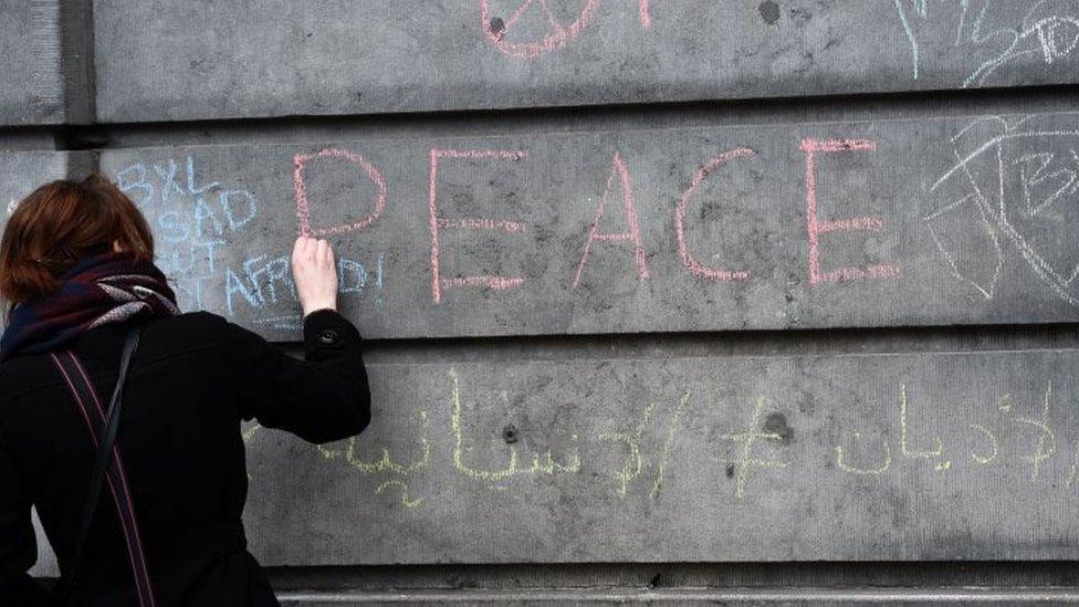 A woman in Brussels writes a message on a wall in tribute to the victims. Photo: 23 March 2016