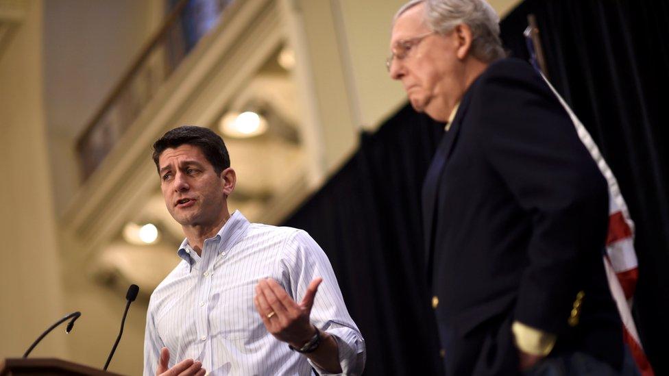 A photo taken at the "congress of tomorrow" event on 27 January, 2017, shows speaker of the house Paul Ryan, photographed from a low angle in sharp focus at a podium, left, flanked by Mitch McConnell slightly out of focus to the right, standing in front of an American flag.