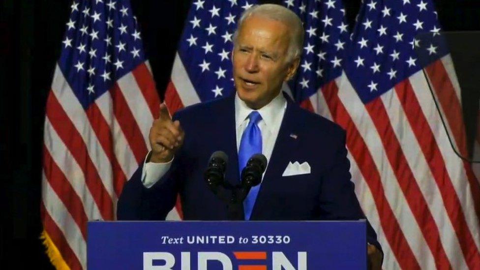 Joe Biden on stage with US flags in the background