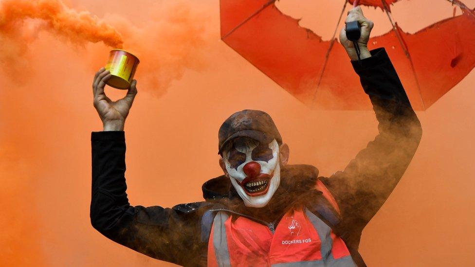 A man wearing a clown mask and waving a smoke bomb takes part in a demonstration to protest against the pension overhauls, in Marseille, southern France, on 5 December, 2019.