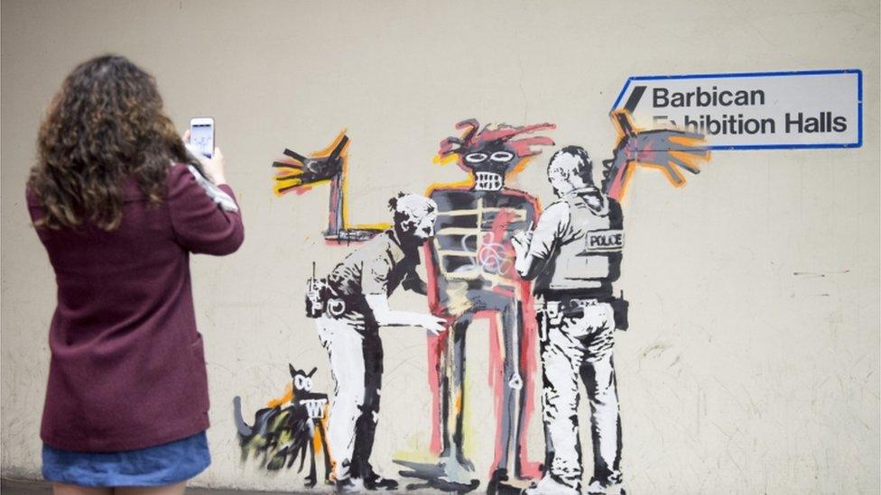 A woman takes a photo of one of two new murals painted by the artist Banksy near the Barbican Centre