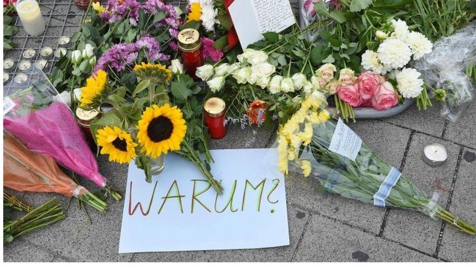 A sign reading "Why" in German lies next to flowers left at the Munich shopping mall in tribute to the victims of the shooting (23/07/2016 )