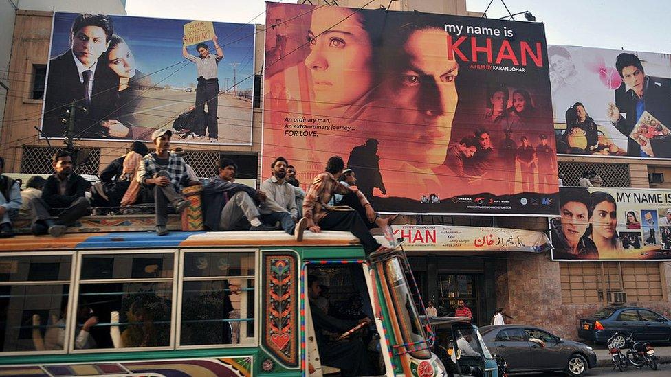 Pakistani commuters, sitting on top of a bus, pass by a cinema screening Indian Bollywood actor Shah Rukh Khan's film 'My Name is Khan' in Karachi on February 12, 2010.