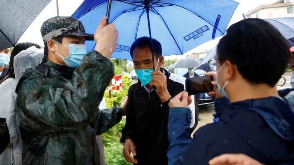 A guard holds an umbrella over the relative of a victim at the village closest to the crash site