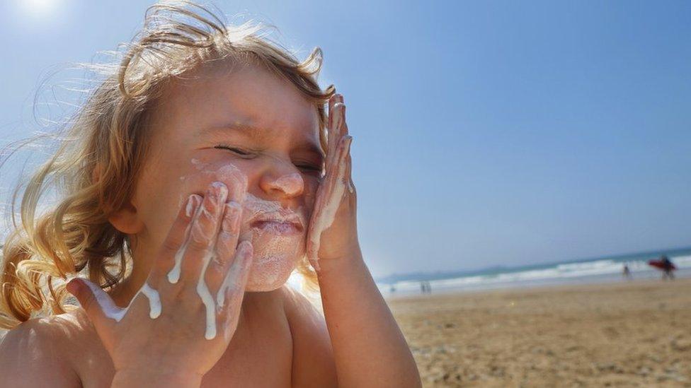 A child putting sun cream on their face at the beach