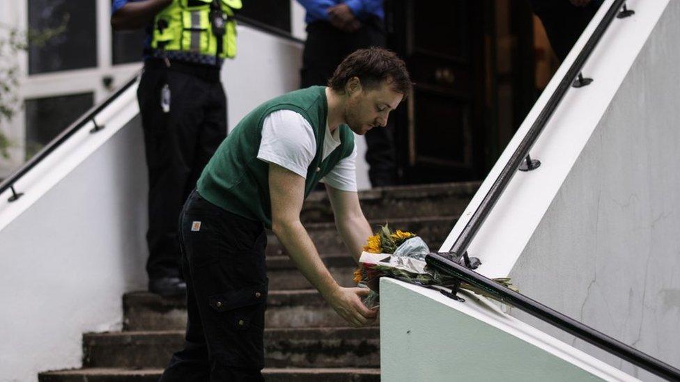 A man places a bouquet of flowers on the steps of the London Irish Centre before attending the vigil inside