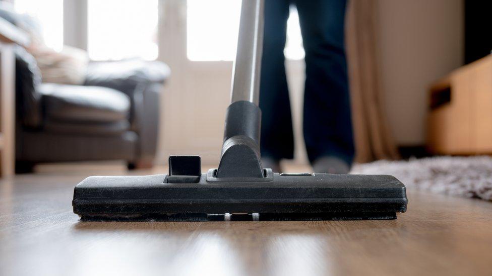 Close-up of a vacuum cleaner being used by a blurred figure (legs only visible)