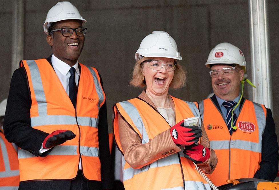 Prime Minister Liz Truss (C) and Britain's Chancellor of the Exchequer Kwasi Kwarteng (L) wearing hard hats and hi-vis jackets, visit a construction site for a medical innovation campus in Birmingham, central England, on October 4, 2022