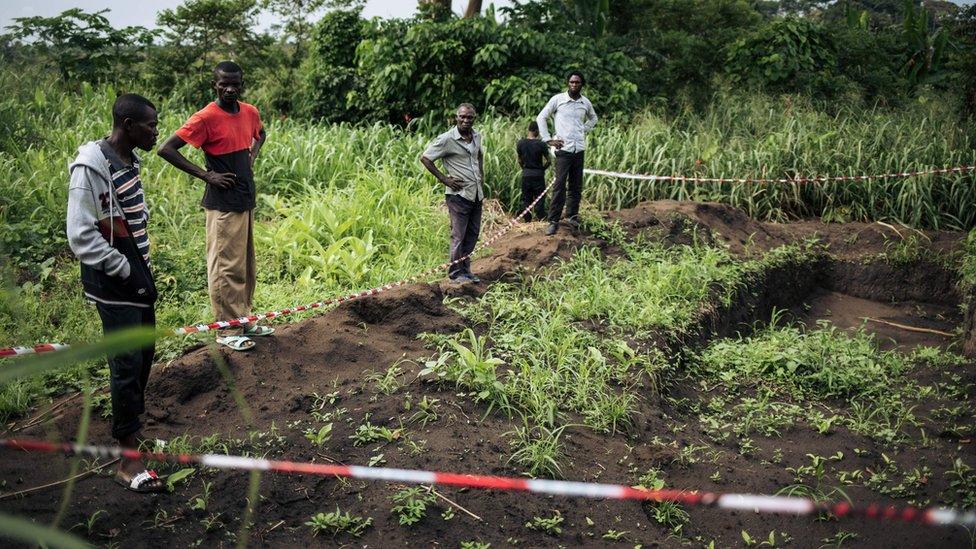 Survivors of an attack in the western village of Bongende, in the Democratic Republic of the Congo, stand on January 27, 2019, next to a mass grave that allegedly contains 100 bodies