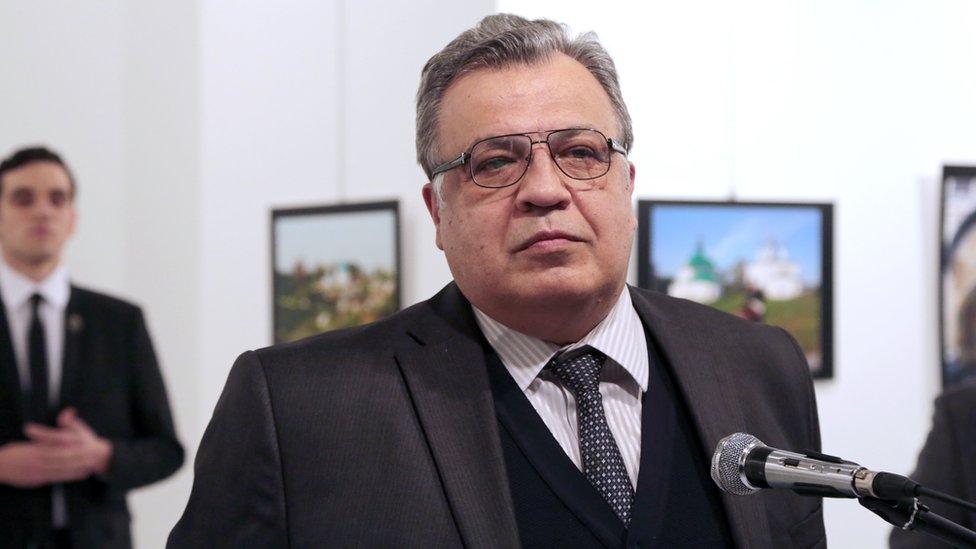 Andrei Karlov, the Russian Ambassador to Turkey, pauses during a speech. His killer stands behind his shoulder in a suit.