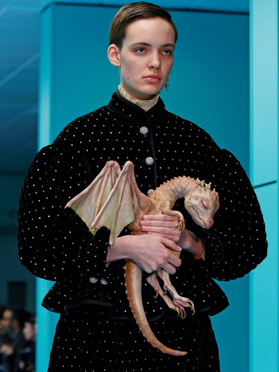 A female model on the catwalk clutching a prosthetic sleeping baby dragon