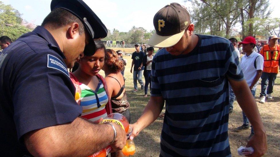 A Mexican police officer pours a soft drink for a migrant