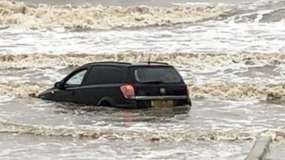 Car submerged in waves on beach