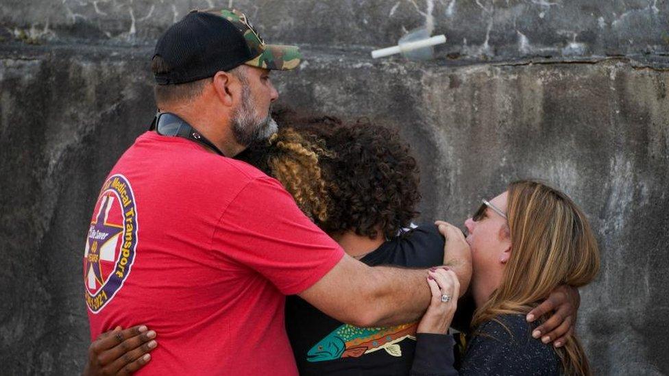 Three people hug each other at a vigil