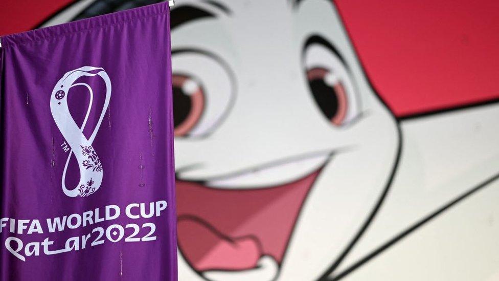 A FIFA banner is displayed in front of a poster of Qatar 2022 mascot La'eeb.