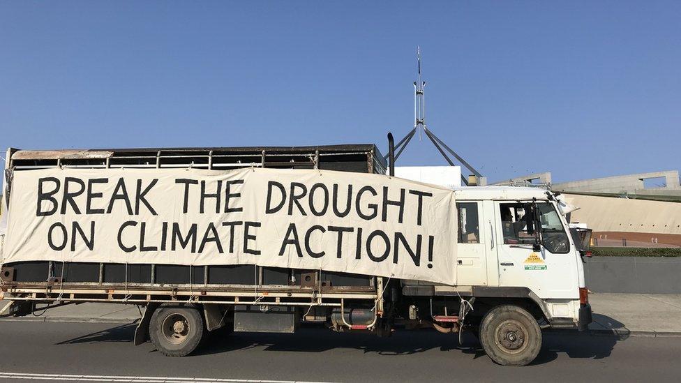 A lorry drives past parliament with a big sign on the side which reads: 'Break the drought on climate action!'