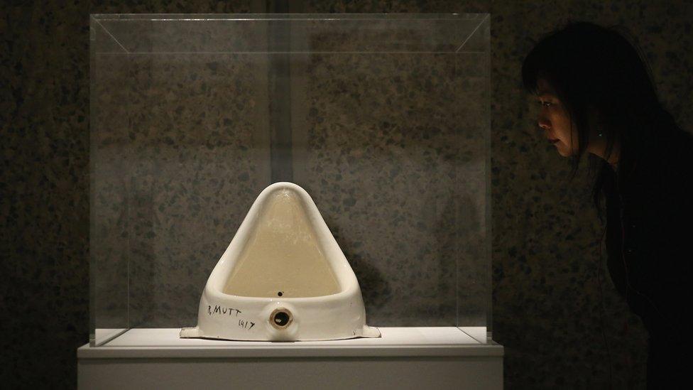 A woman looking at Duchamp's artwork "Fountain" at the Barbican Art Gallery, 2013