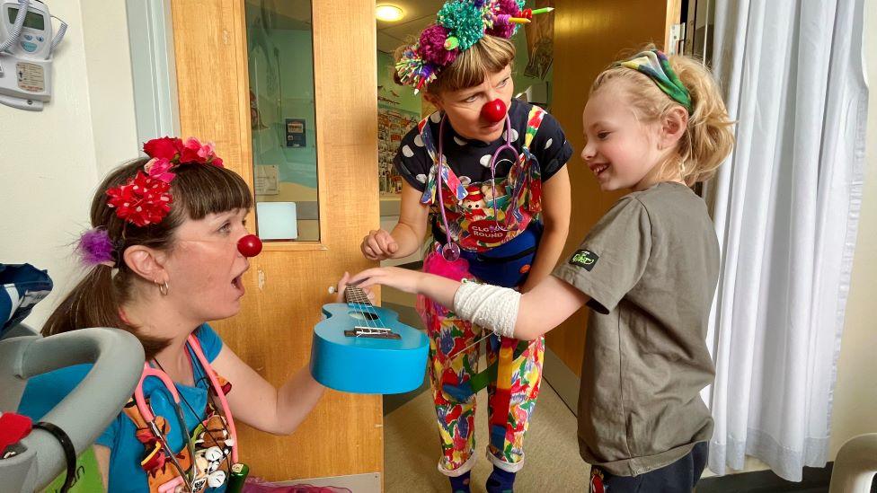 Doctor clowns performing for a little boy in hospital who is laughing.