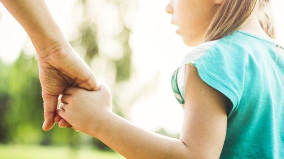 Posed photograph of a child holding hands with an adult