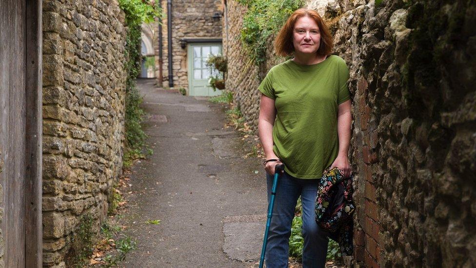 Woman leaning against a wall in a lane wearing a green t-shirt