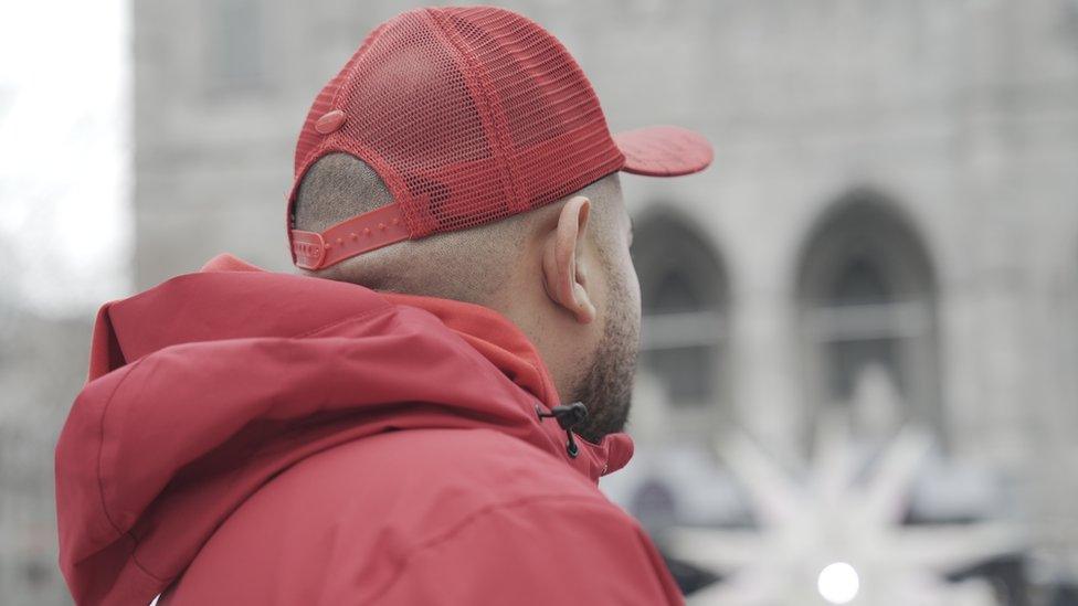 A photo of the back of Joshua's head in downtown Montreal. He is wearing a red baseball cap and parka.