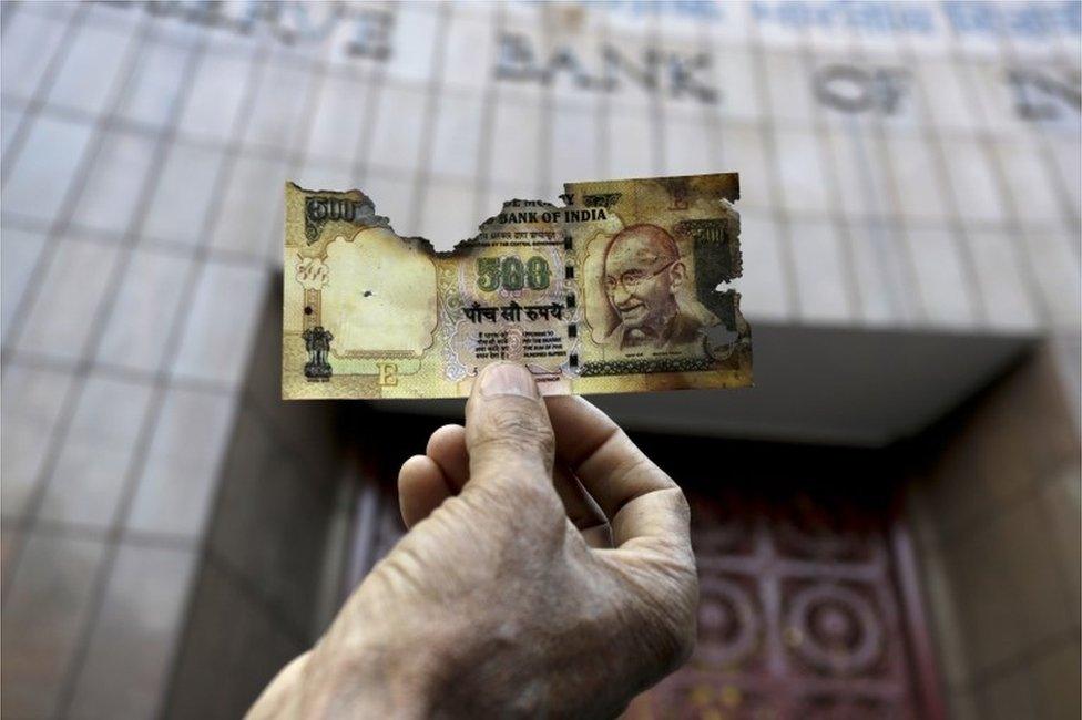 In this Nov. 16, 2016 file photo, a man holds a charred facsimile of the discontinued Indian currency 500 note after a protest by a traders association demanding adequate arrangement to exchange discontinued currency notes outside Reserve Bank of India in Kolkata, India.