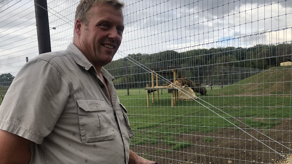 Andy Johnson in a khaki shirt in front of a mesh fenced animal enclosure